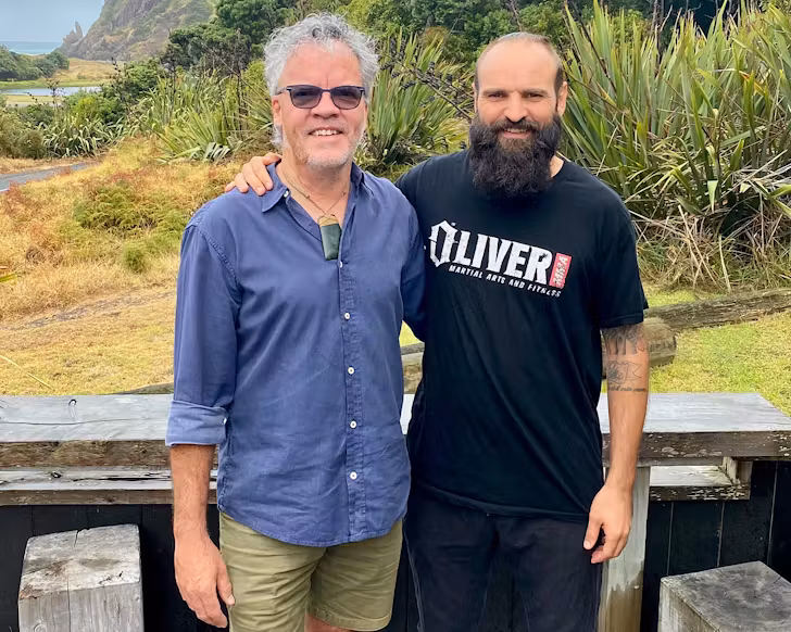 Peter Gordon and Lucas Parkinson stand on Aryeh's deck with an arm around each other's shoulders. 