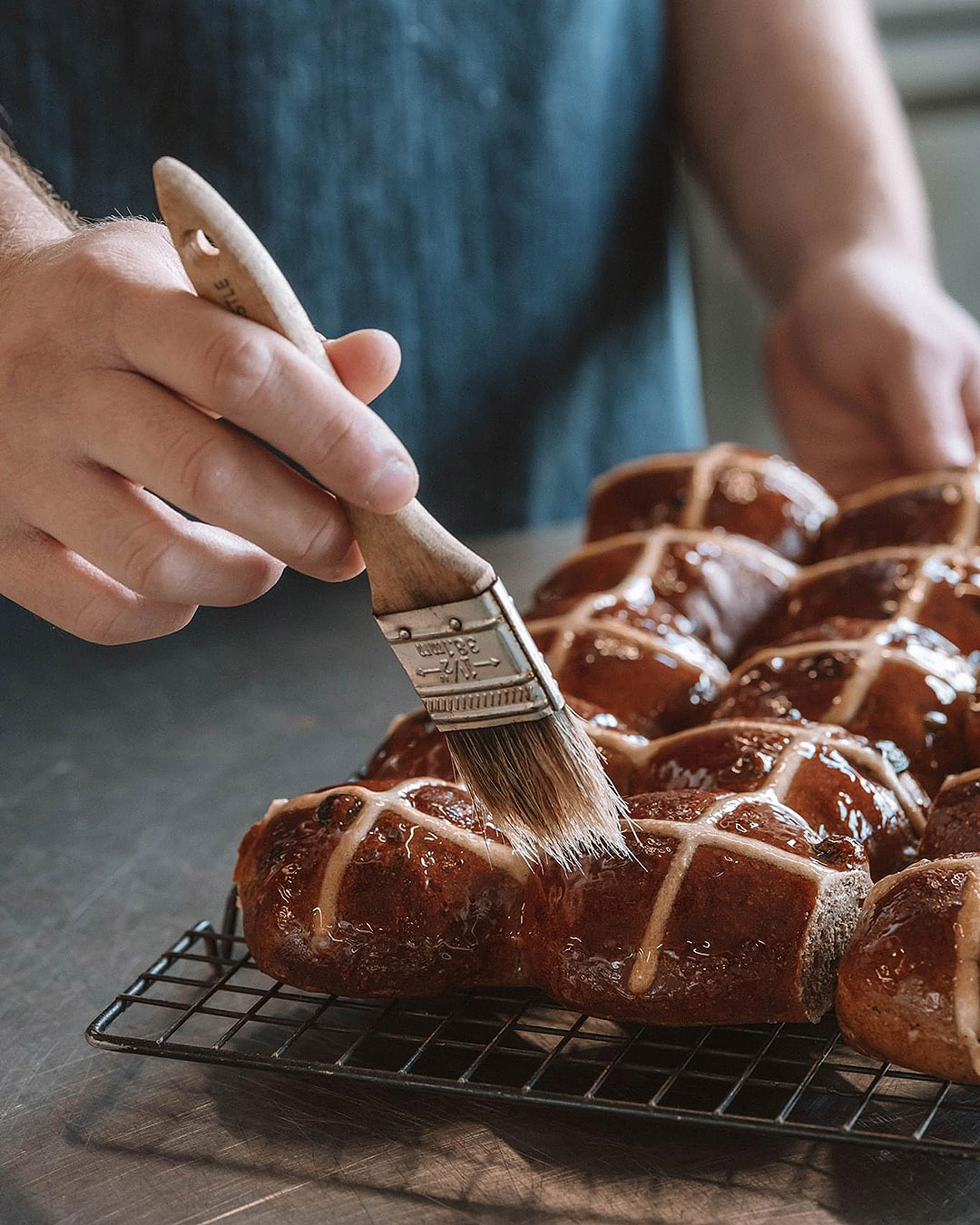 Someone glazes delicious looking hot cross buns.