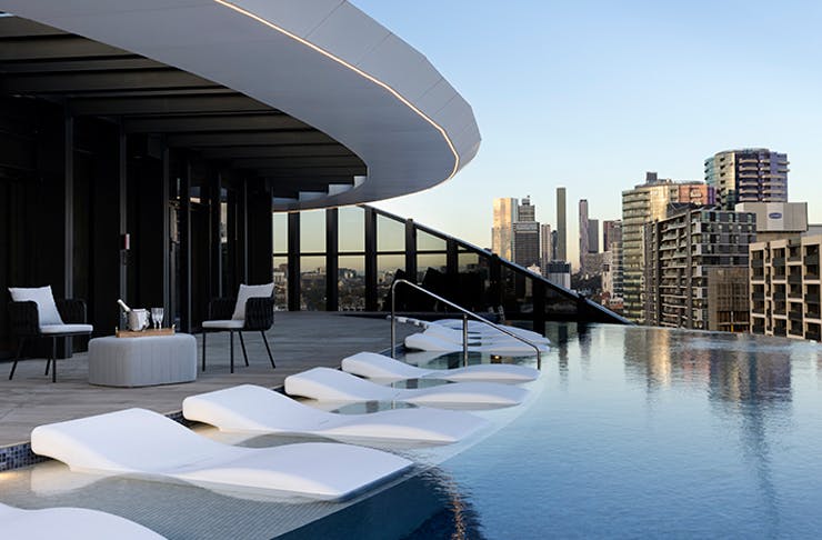A shot side on of an infinity pool with pool chairs that look out onto the city. 