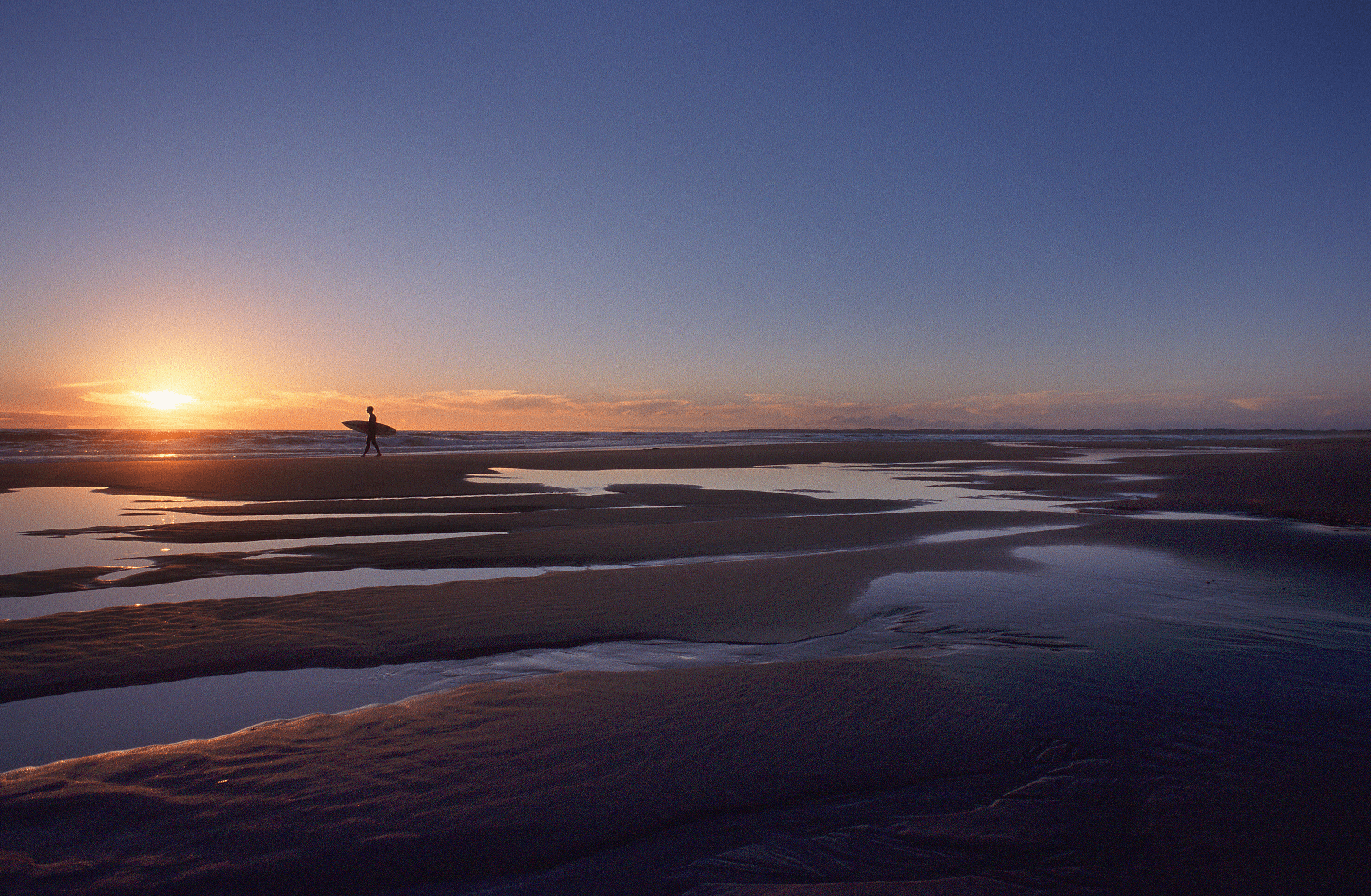 A surfer walking across the beach at one of the best walks in Victoria. 