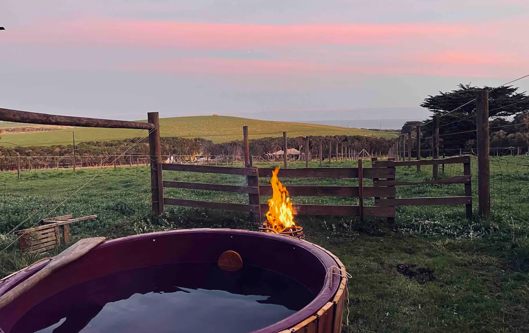 An outdoor hot tub at dusk with a fire at a glamping Victoria spot. 