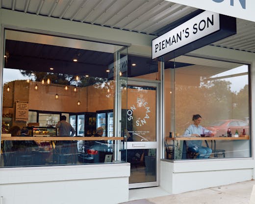 The shopfront of a bakery with a person sitting in the window. 