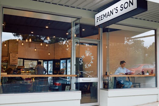 The shopfront of a bakery with a person sitting in the window.