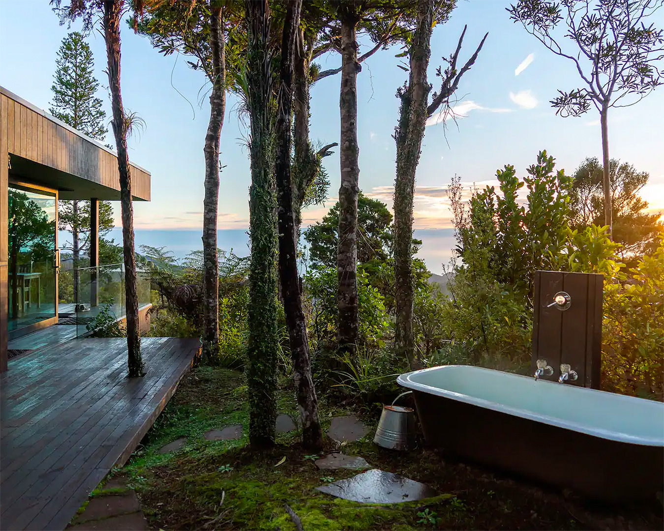 Chic black wooden house with deck surrounded by native trees and ferns. 