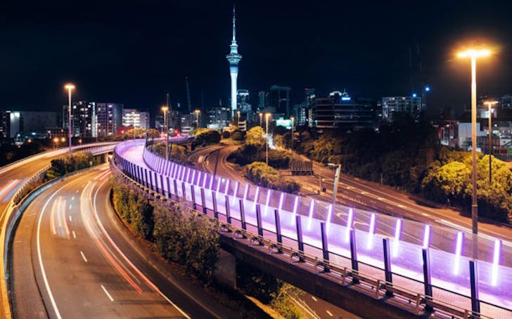 Evening view of Te Ara I Whiti, Pink Light Path from afar lit up with the sky tower in the background