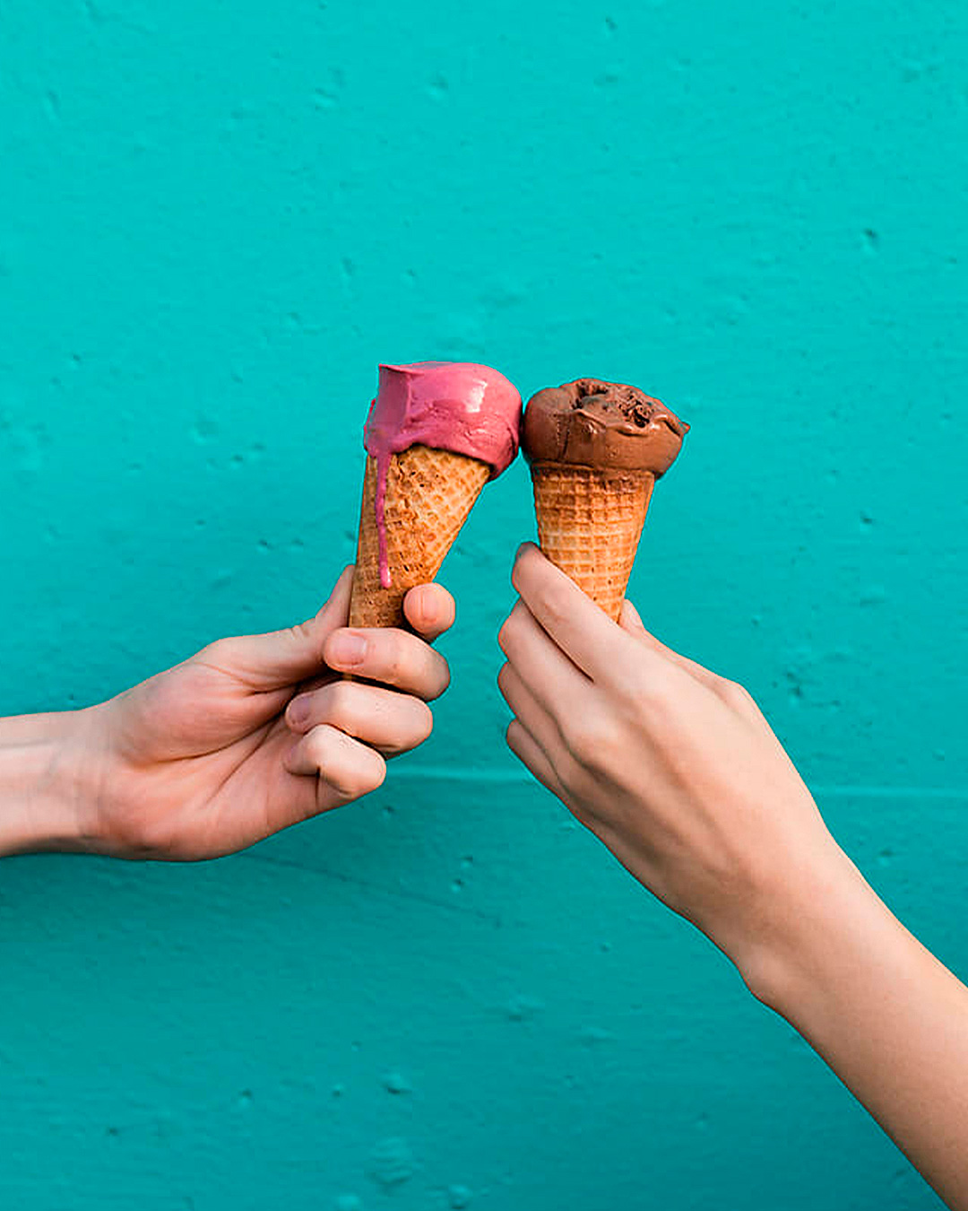 Two people hold up Pistackio gelato in front of a green wall, one of the best gelato shops in Auckland.