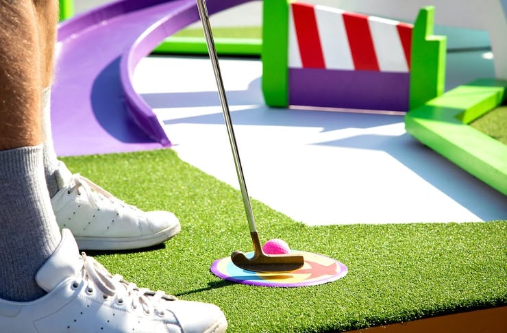 A person in white sneakers playing putt putt golf at Pixar Putt in Sydney. 