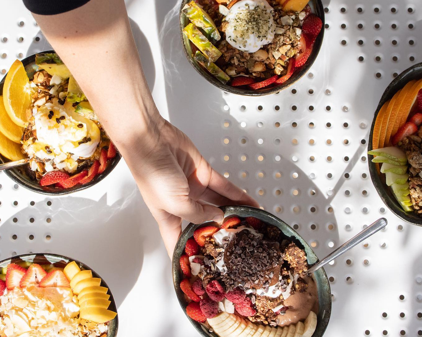 Hand holding a smoothie bowl above a table with various other smoothie bowls