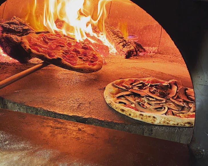 Two pizzas in a flaming pizza oven.