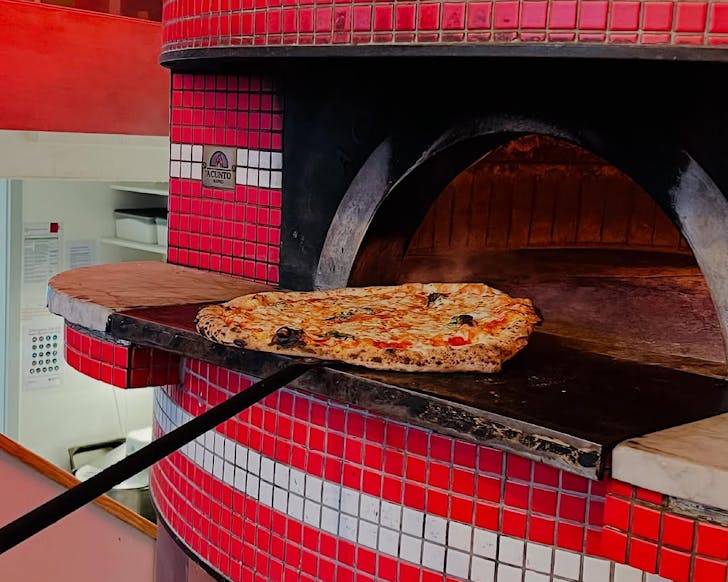 A pizza is slid into a classic red tiled pizza oven.