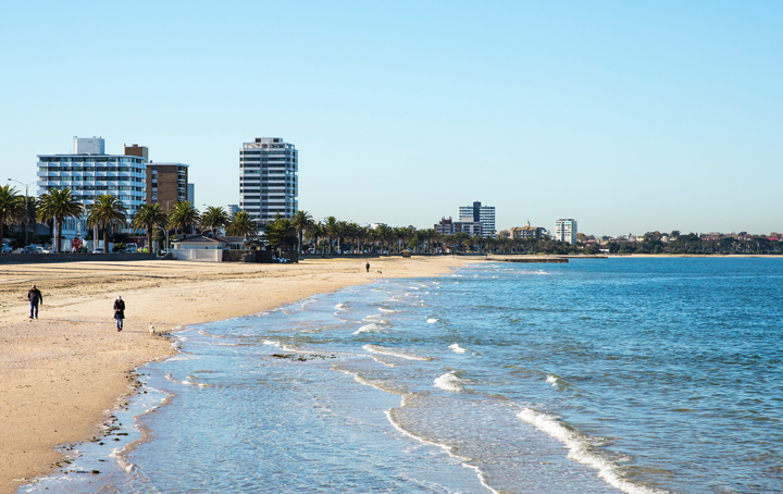 A wide-shot of Port Melbourne beach with people walking on the sand. 