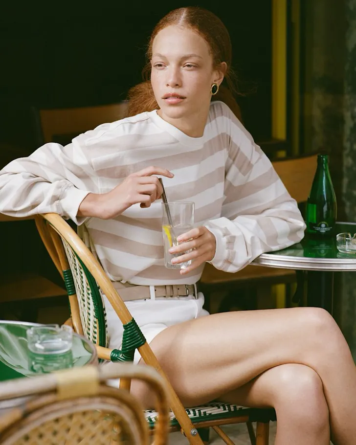 A woman sits at a table in shorts and a striped top from Posse one of the best Australian fashion labels