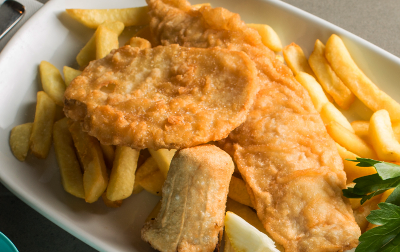 A plate of fried battered potato cakes, dim sims and fish. 