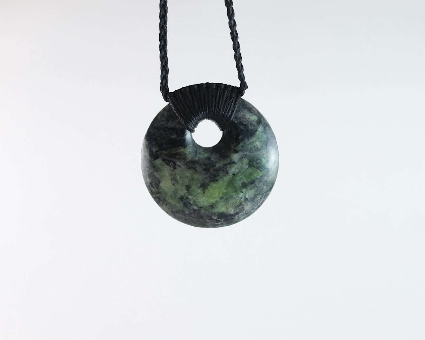 A circular greenstone pounamu pendant with a hole in the middle of it hangs on a necklace string.