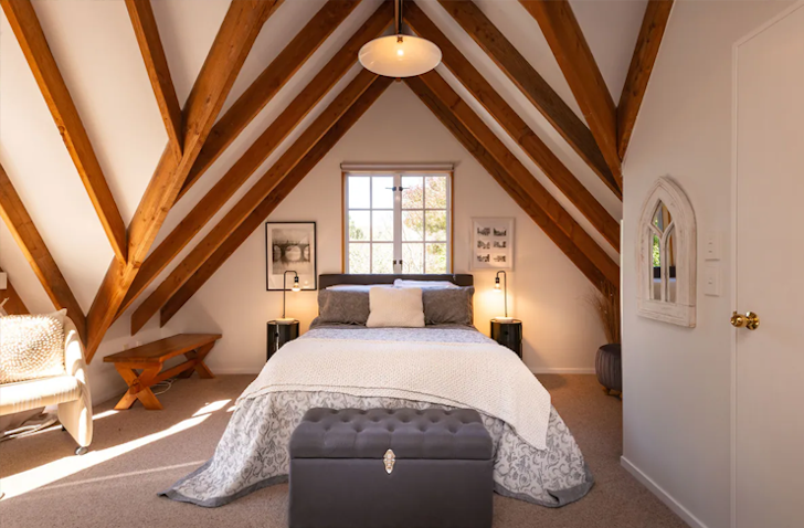 A large bed in an A-frame bedroom with a striking geometric ceiling pattern made from wooden beams. 