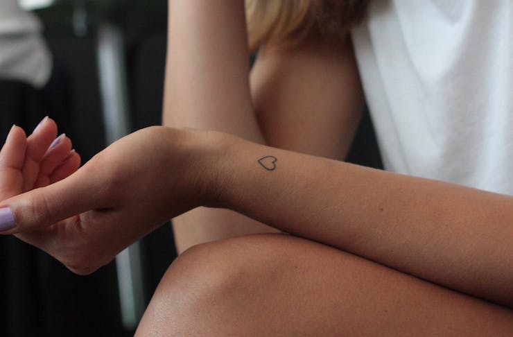 A girl's arm with a small fine line tattoo of a heart on her wrist