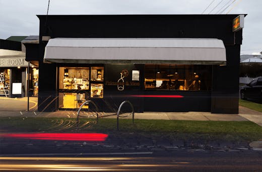 The shop front exterior of a wine bar with people dining inside. 