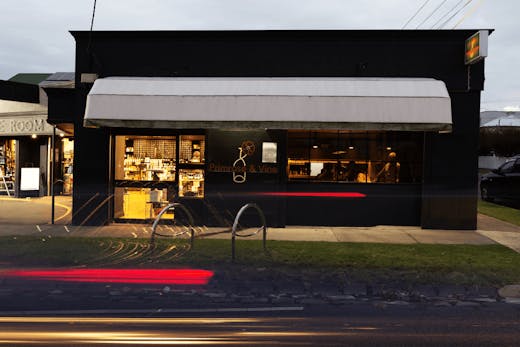 The shop front exterior of a wine bar with people dining inside.