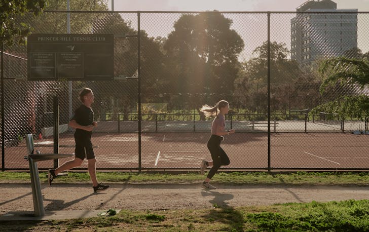 Two people walking across a tennis club with the sun shining on one of the best runs Melbourne. 