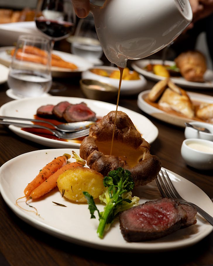 Someone pours gravy over a large Yorkshire pudding. 