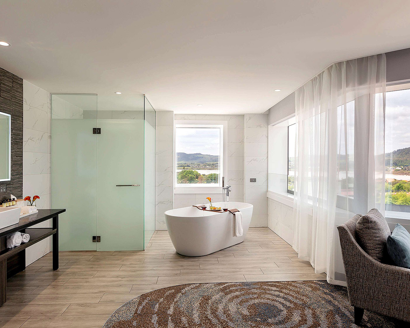 A fancy hotel room with a sleek stone bath, with stylish wooden tray for holding your wine, in the centre. 