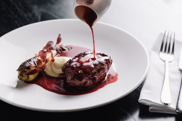 A person pouring sauce over a piece of beef at one of the best restaurants in Southbank.