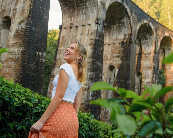 A woman in a white top and orange skirt take in the view of an ancient ruin.