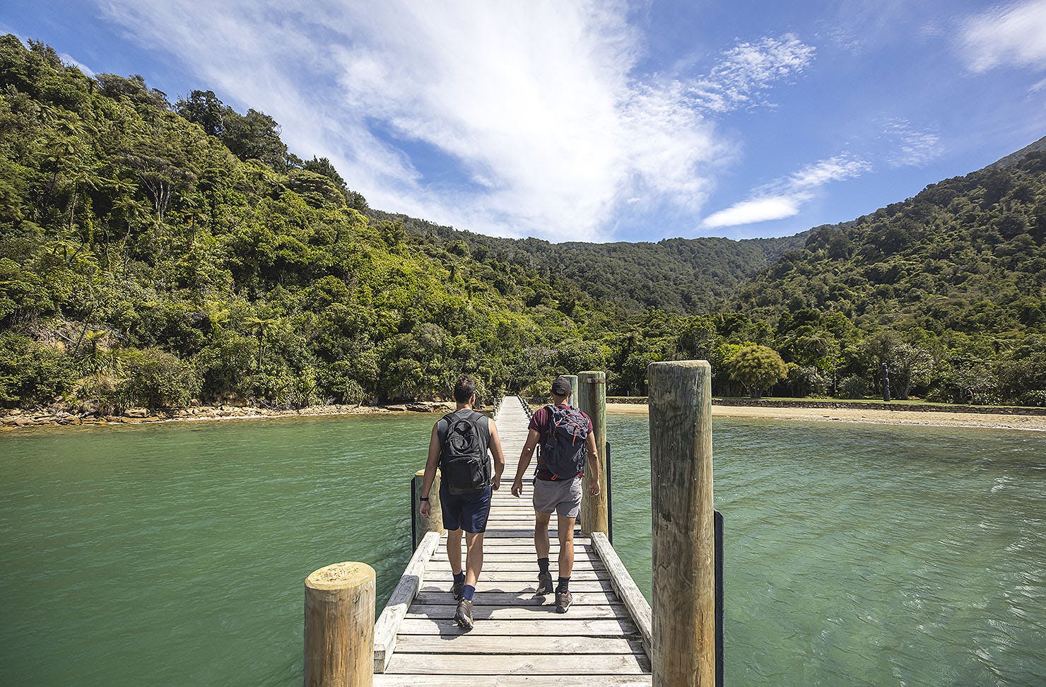 Two people walk along a jetty while walking The Queen Charlotte Track.