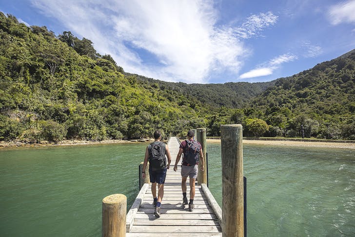 Two people walk along a jetty while walking The Queen Charlotte Track.