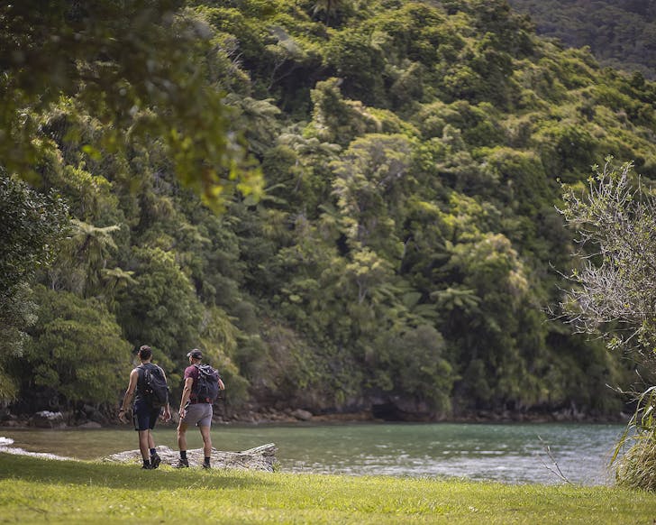 Two people walk by the water on The Queen Charlotte Track.