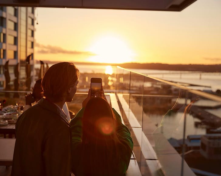 A couple take a photo as the sun sets at Queens Rooftop & Wineshop. 