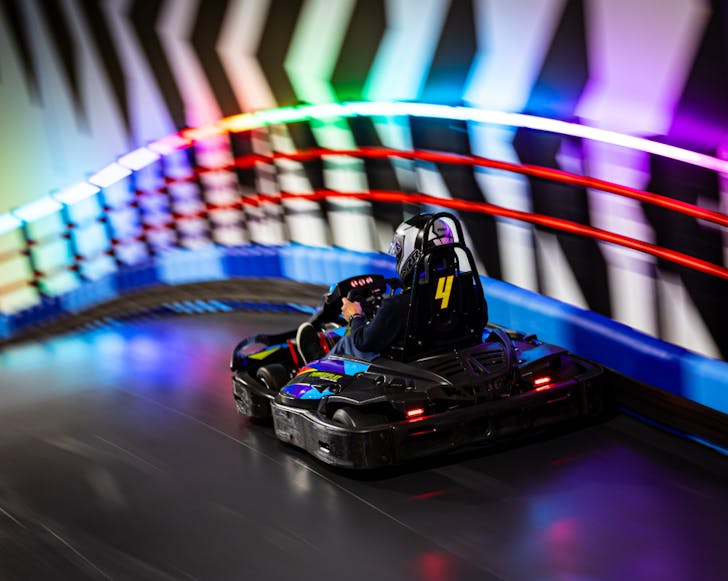 A go-kart rider lit up by flashing neon lights on the track