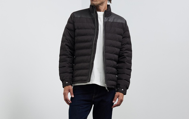 A person in a white t-shrt and a black quilted jacket, one of the best men's puffer jackets. 