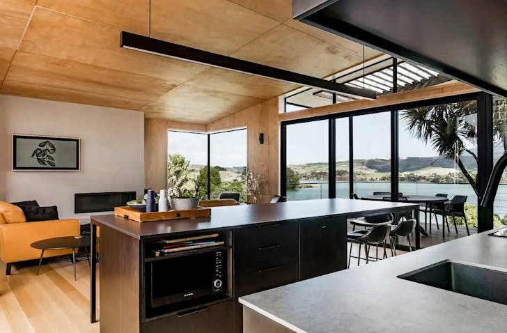A modern kitchen looks out onto a spacious dining room and view of Mt Karioi at this Raglan airbnb. 