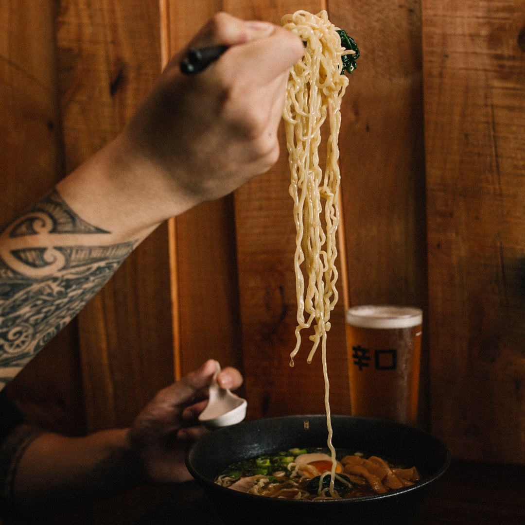 A person gets stuck into a bowl of Ramen Takara's ramen, pulling up noodles with their chopsticks. 