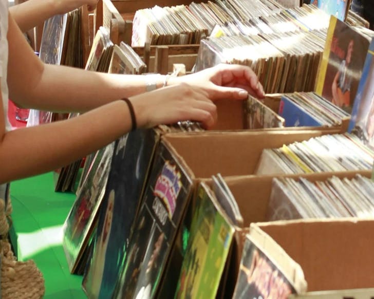 A close up image of a pair of hands searching through a crate of vinyl records.
