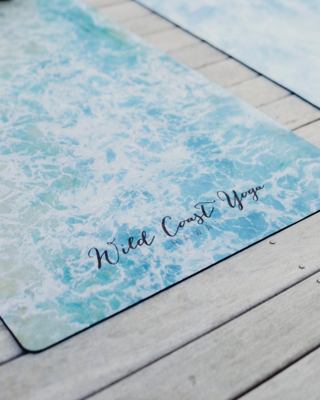 The edge of a yoga mat covered in a wave print with ‘Wild Coast Yoga’ written on it. 