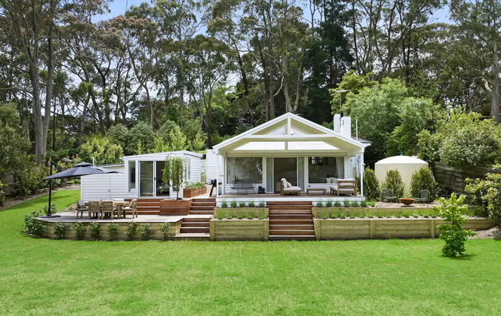 A large white house with multi-level deck and sprawling grass.