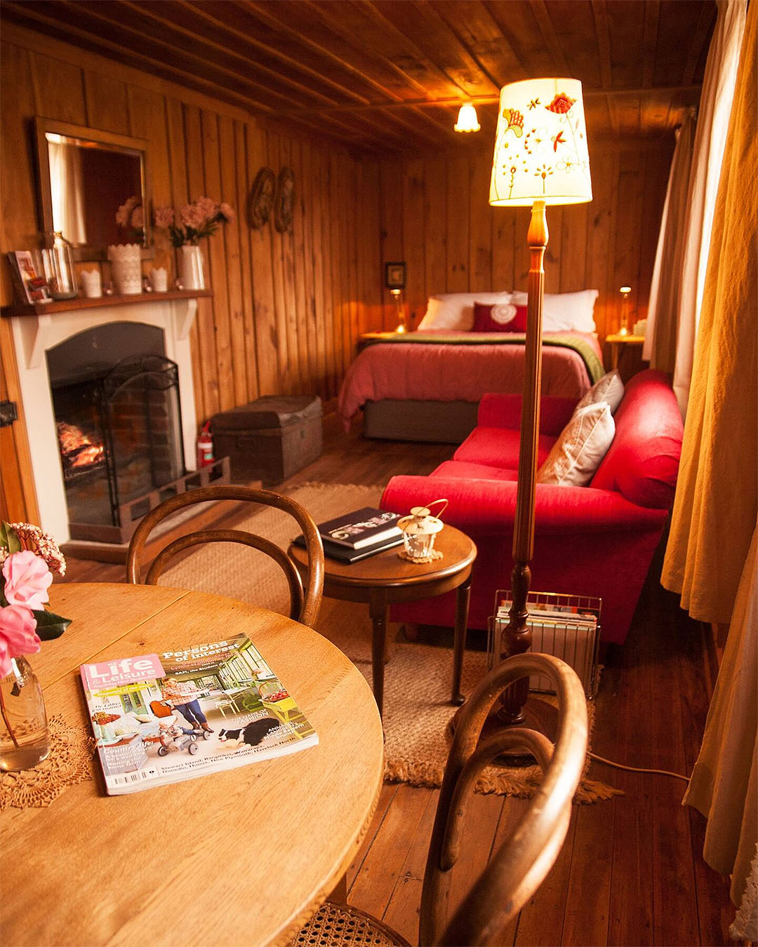 A cosy bedroom at Red Cottages showing vintage furnishings and a wood-burning fireplace.