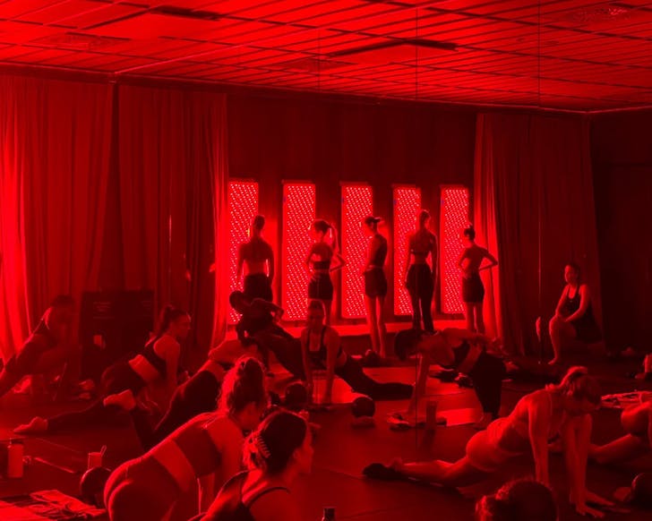 People stand in front of the red light therapy panels while other people stretch on the floor. 