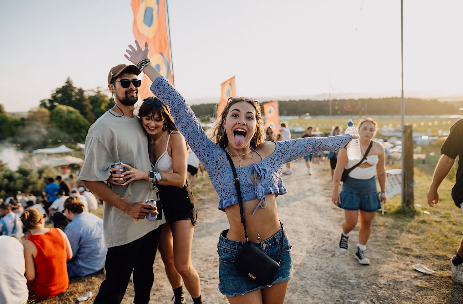 A woman in a purple crop top and jean mini skirt sticks her tongue out happily.