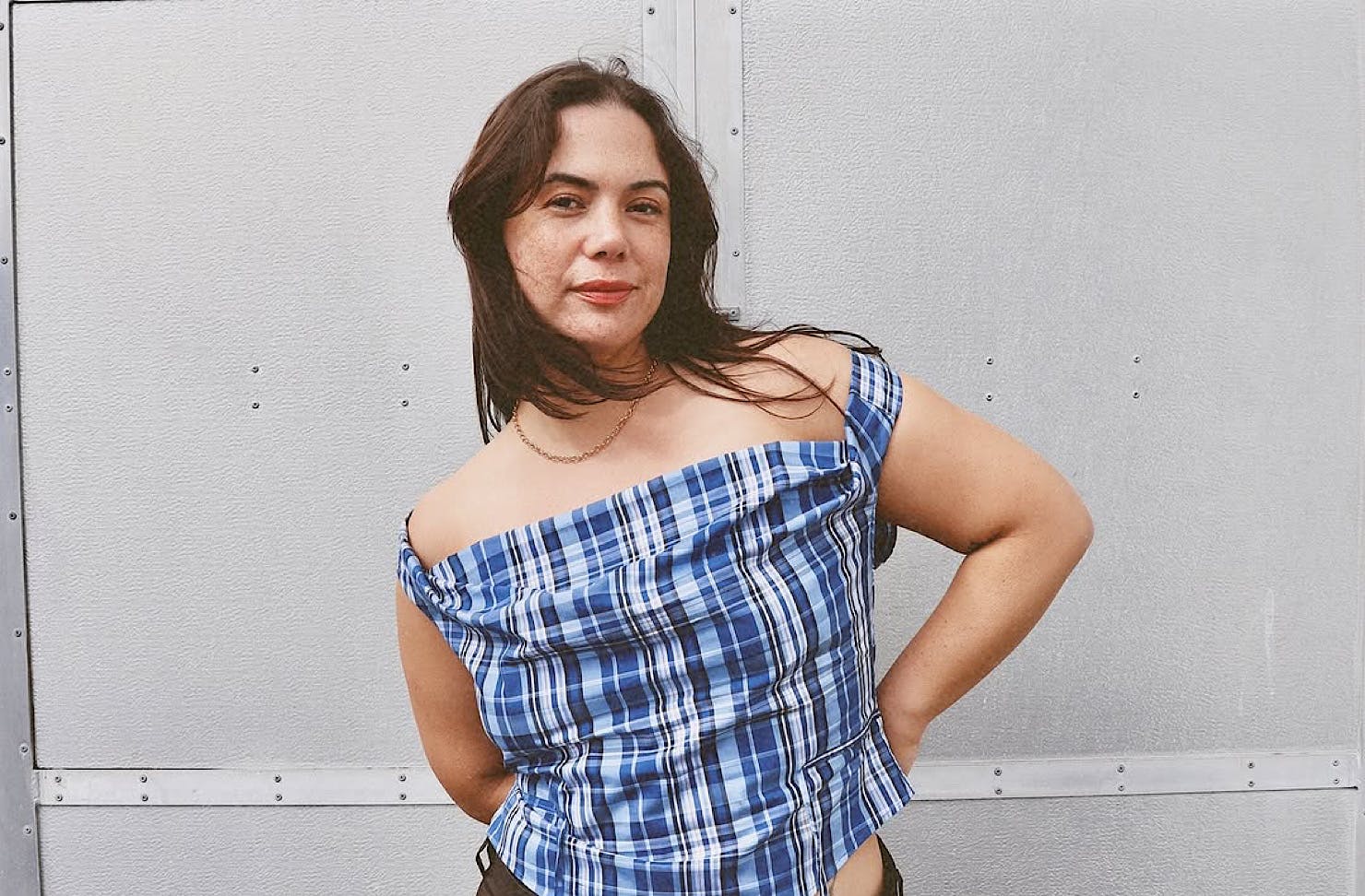 A woman wears an off-the-shoulder blue and black chequered top by Riel, one of NZ's best sustainable fashion labels. 