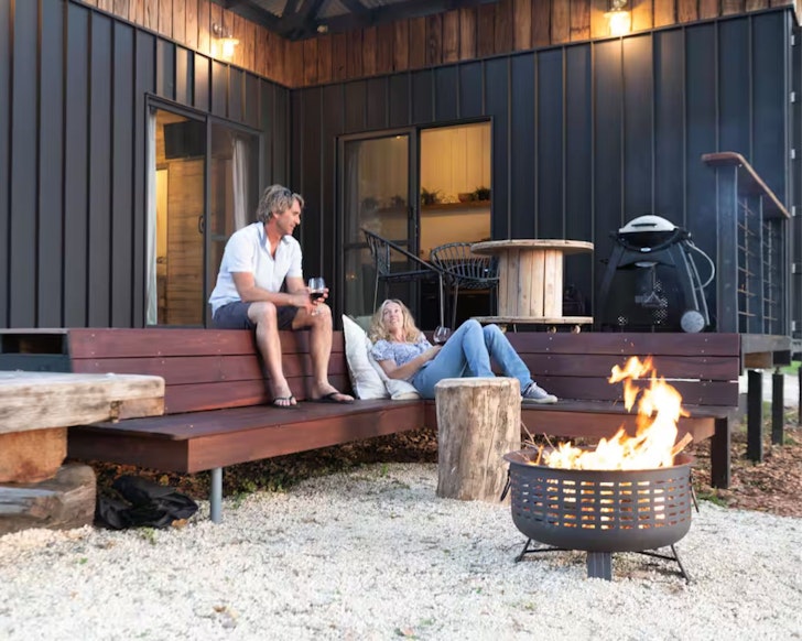 Two guests lounge by the fire pit at River's End Retreat one of the best tiny houses in Australia