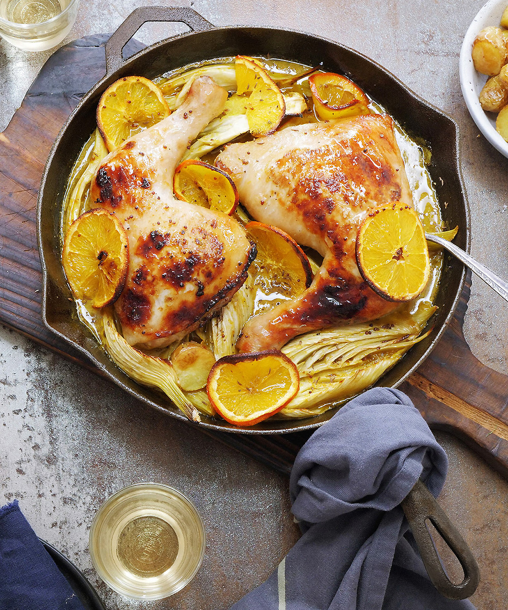 A cast-iron skillet dish with appetising chicken and lemon on a tabletop.