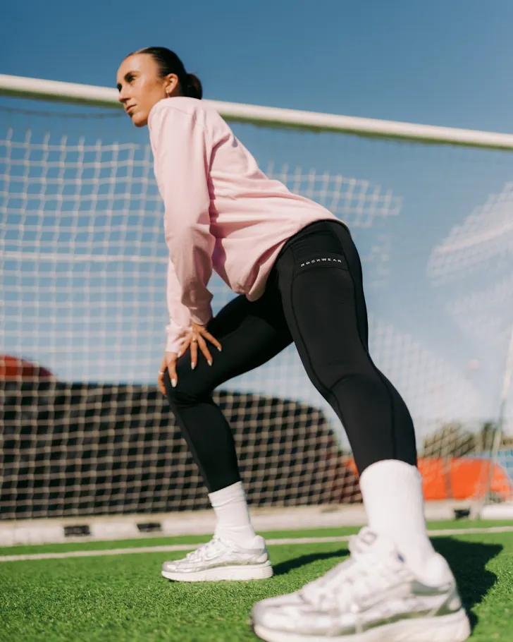 A woman stands in front of a goalpost wearing clothes from Rockwear one of the best activewear brands