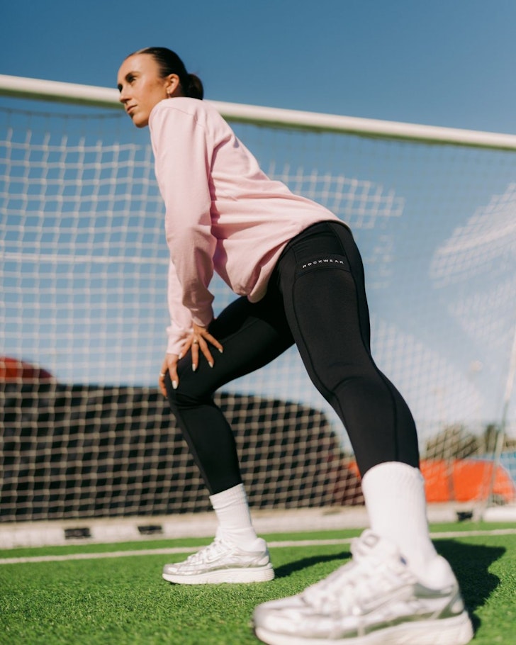 A woman stands in front of a goalpost wearing clothes from Rockwear one of the best activewear brands