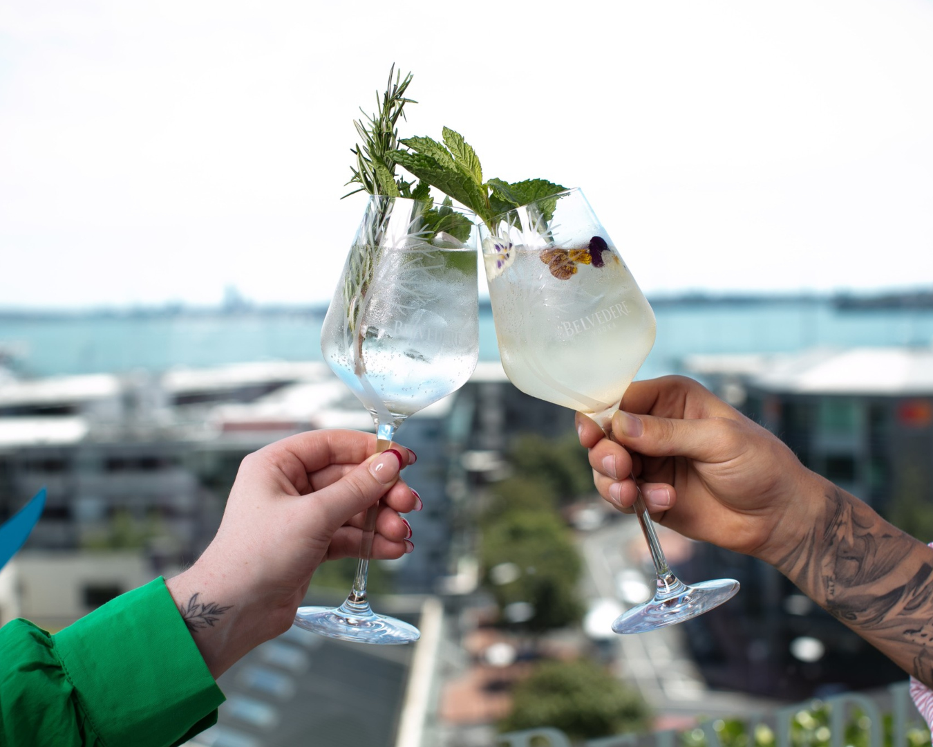 A couple clink glasses filled with cocktails on a rooftop.