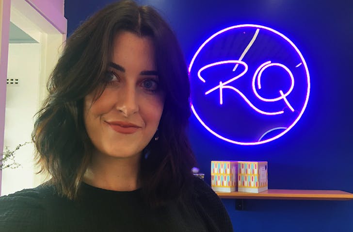 Michaela stands in front of a Rose Quartz neon logo