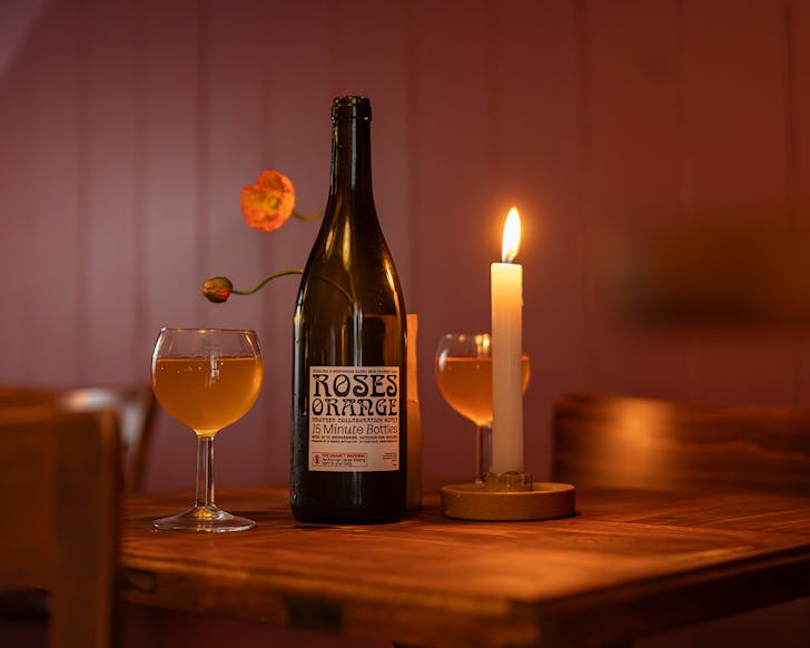 A bottle of Roses orange wine on a candlelit table with two full glasses. 