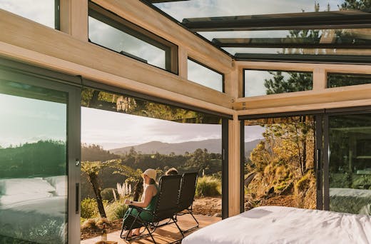 Two people sit on a deck and look out over an incredible view of the Karangahake Gorge. 
